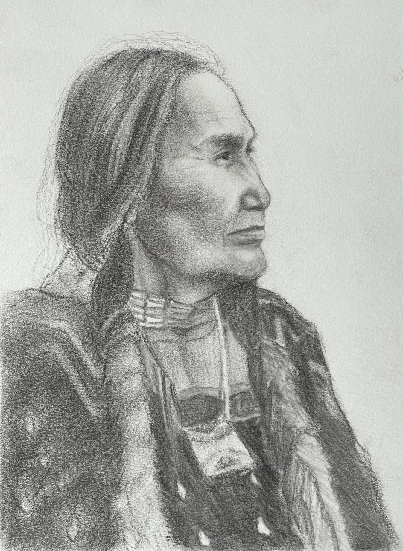 Older Native American woman portrait in profile looking off to the right. Her hair is braided and she is wearing a traditional shirt and a pouch around her neck.