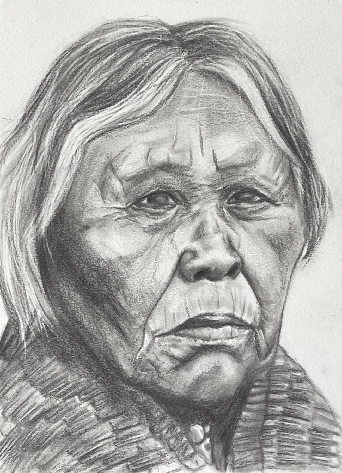 Portrait of an older Native American woman looking almost straight-on with gray hair, wearing a shirt made of reeds.